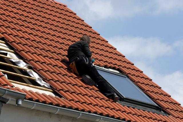 Installing roof windows by worker on a tiled roof.